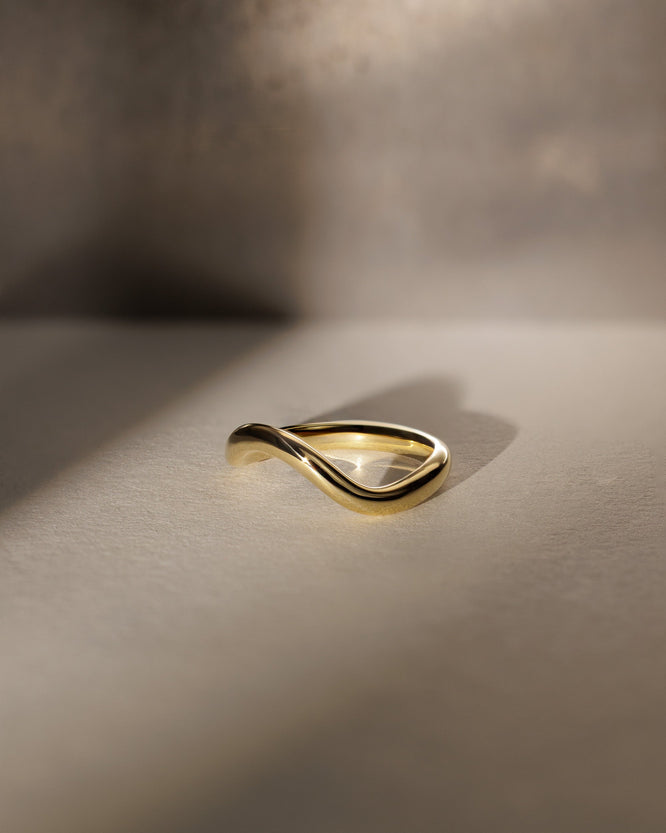 Plain curved wedding band with a smooth polished finish β minimalist contour design in gold, perfect for pairing with solitaire or vintage engagement rings.